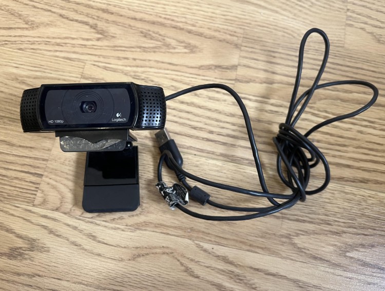 Logitech HD 1080p USB video camera placed on a wooden floor with cable coiled beside it.
