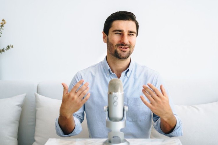 Liam Austin recording a podcast using a Blue Yeti microphone while seated in a bright, minimal setup.