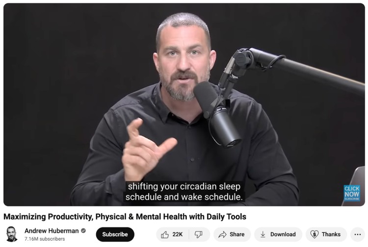 Andrew Huberman sitting at a desk speaking into a microphone during a recording, demonstrating a clean and professional studio layout often used in a great podcast.