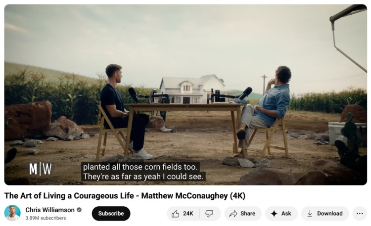 Chris Williamson and Matthew McConaughey recording an outdoor interview at a wooden table in a cornfield, creating a cinematic scene that feels like the perfect podcast setting.