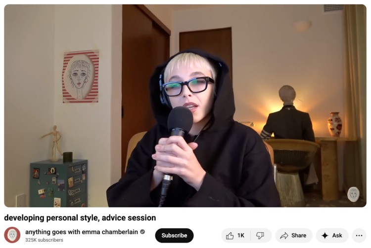 Emma Chamberlain recording her podcast in a dimly lit room with a warm, cozy type of background featuring soft lighting, decor, and a relaxed home-studio vibe.