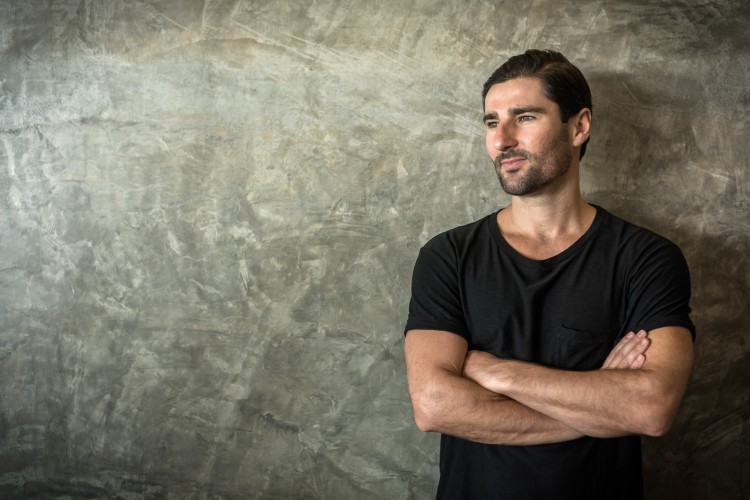 Liam Austin standing against a textured wall with arms crossed, used as a profile image for podcast marketing content.