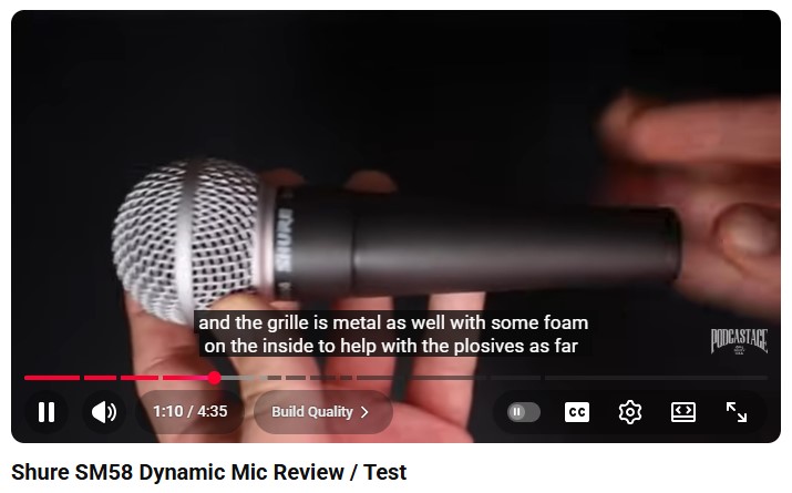 Close-up of a Shure SM58 dynamic microphone being held during a hands-on review, showing the metal grille and body design.